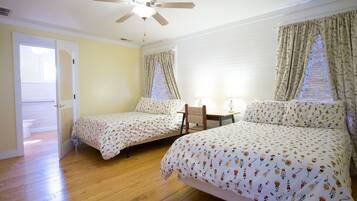 Un dormitorio con dos camas, ventilador de techo, piso de madera y ventana con cortinas.