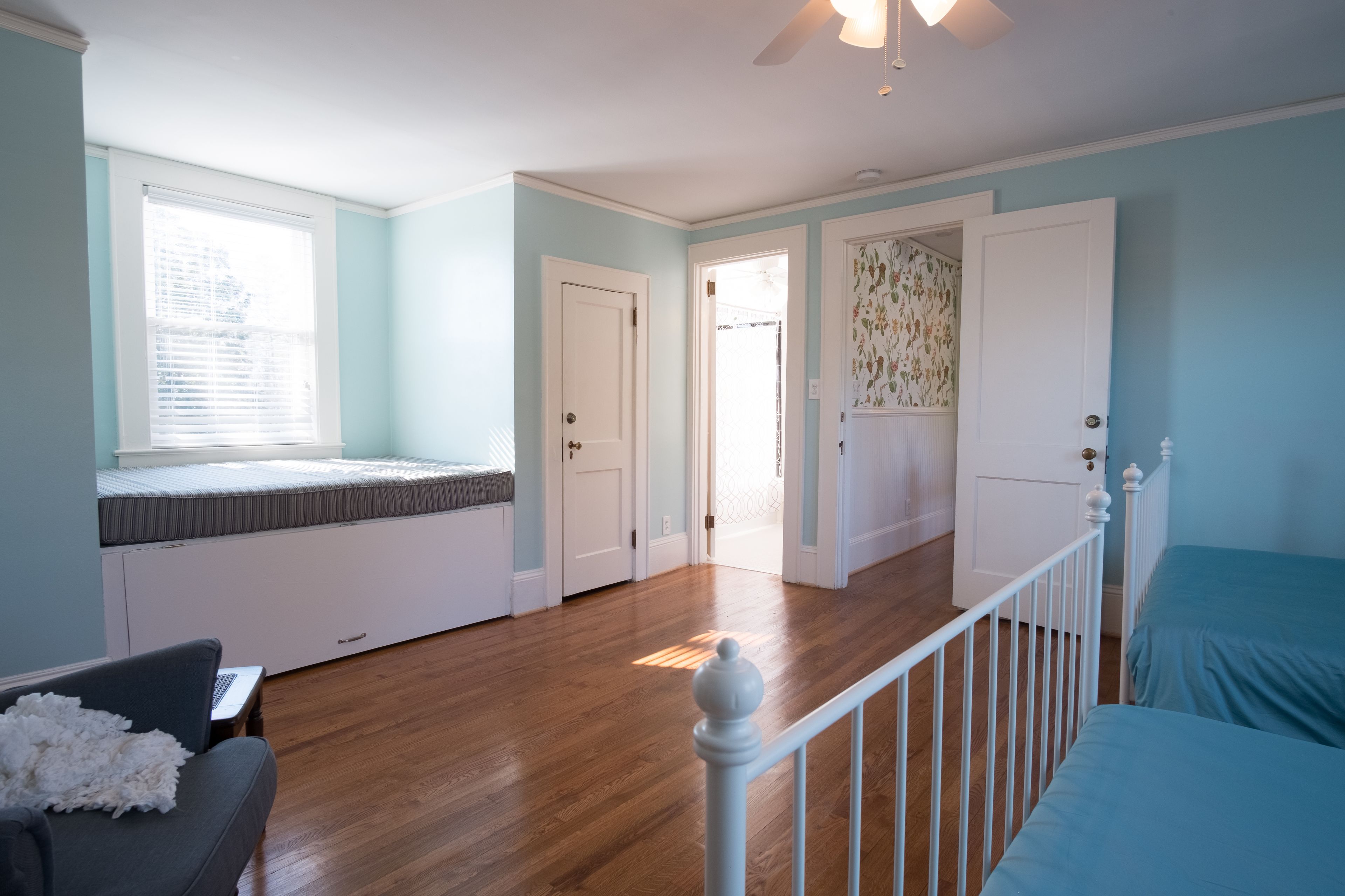 A room with a bed, a window with blinds, a door, and a staircase.
