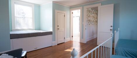 A room with a bed, a window with blinds, a door, and a staircase.