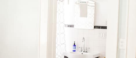 A narrow hallway leading to a bathroom with a white sink, a toilet, and a trash bin.