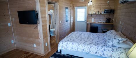 A wooden cabin bedroom with a bed, a television, a microwave, and a small kitchenette.