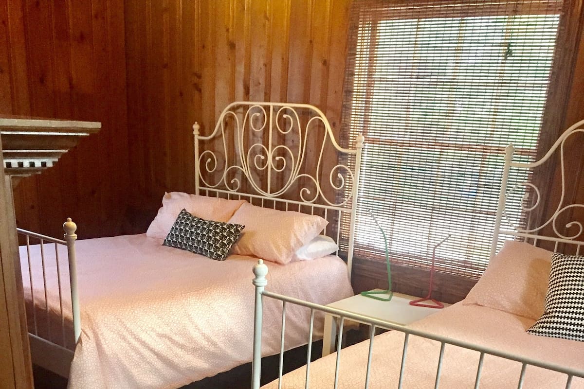 A room with two beds, wooden flooring, and a window with blinds.