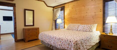 A bedroom with a wooden ceiling fan, a bed with floral bedding, a nightstand with a lamp, and a dresser.