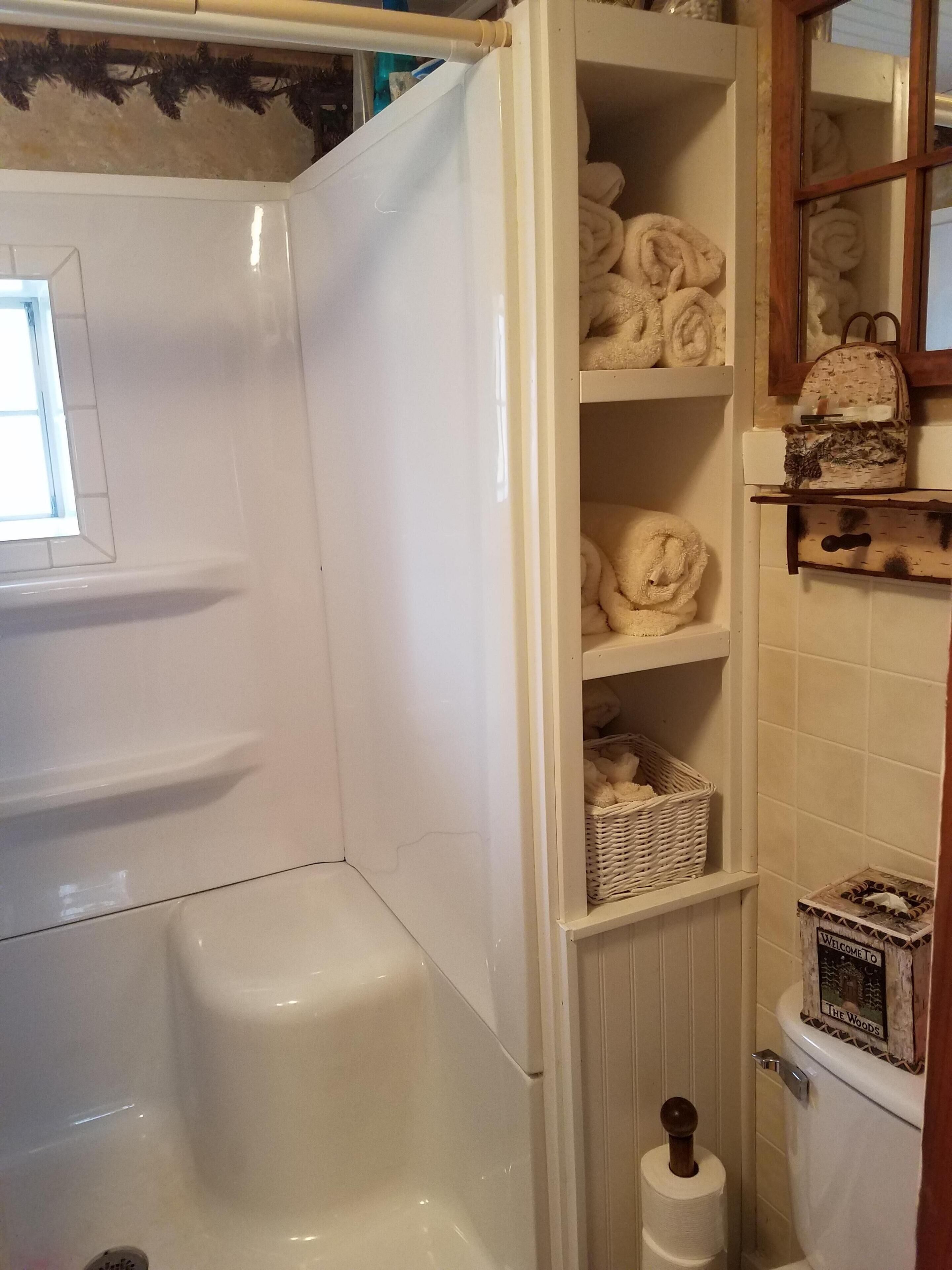 Et badeværelse med badekar, hylder med håndklæder, en fletkurv og et toilet med en dekorativ skilt.