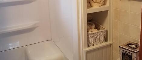 Et badeværelse med badekar, hylder med håndklæder, en fletkurv og et toilet med en dekorativ skilt.