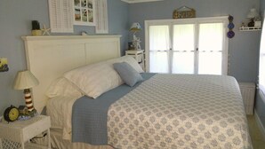 A bedroom with a bed, a nightstand, a lamp, a wall clock, a window with curtains, and a decorative sign. -  Perfect getaway for couples ! close to Ludington!

 (Fountain)