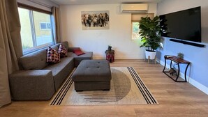 A modern living room with a grey sofa, ottoman, and a flat-screen TV mounted on the wall.