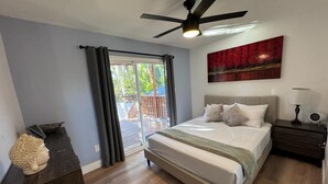 A bedroom with a bed, a ceiling fan, a nightstand, a lamp, and a window with curtains.