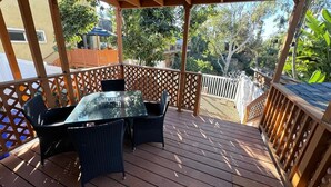 A covered outdoor deck with a table and chairs, surrounded by wooden railings and lattice panels.
