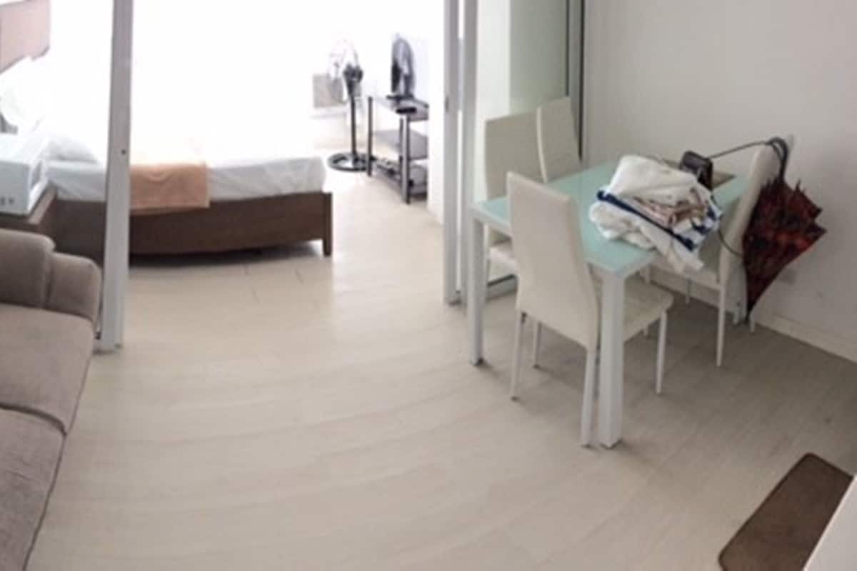 A modern hotel room with a beige sofa, a small desk with a chair, and a bed in the background.