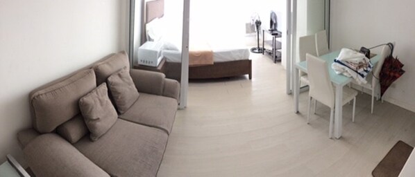 A modern hotel room with a beige sofa, a small desk with a chair, and a bed in the background. - (Parañaque)