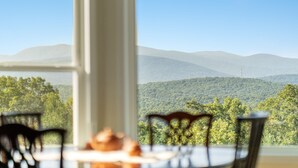 A dining area with a table and chairs, a window with a view of a mountain range and forest. - Shenandoah mountain view home King bed StarLink EV port river access 90 min DC  (Bentonville)