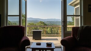 A room with two red armchairs, a small table, and a view of a wooden deck and mountains through large windows. - Shenandoah mountain view home King bed StarLink EV port river access 90 min DC  (Bentonville)