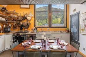 A kitchen with a dining area, a stove, oven, and a window with a view of a forest. - Galena Chalet – 1BR Sleeps 4 - Rare Find Retreat (Telluride)
