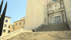 A historic building with a tall tower and a large circular window at the bottom of a set of stone steps leading up to the entrance. - Charming flat next to the Cathedral (Girona)
