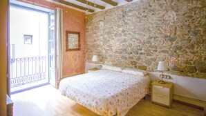 A bedroom with a stone wall, wooden floor, and a bed with two bedside tables. - Charming flat next to the Cathedral (Girona)