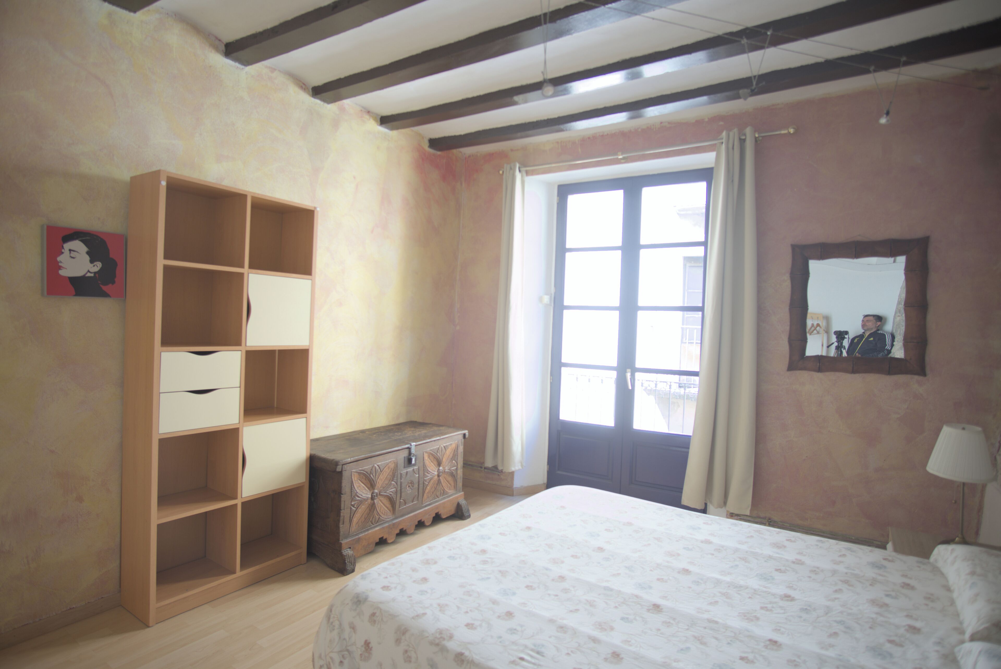 Un dormitorio con una cama grande, un armario de madera, un aparador y una ventana con cortinas.
