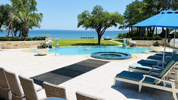 A pool area with lounge chairs, a hot tub, and a view of the sea.
