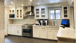 A modern kitchen with white cabinetry, a stainless steel range hood, a built-in microwave, and a window overlooking a snowy landscape.