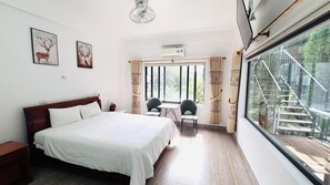 Une chambre avec un grand lit, deux chaises, une petite table et une fenêtre donnant sur un escalier et de la verdure.