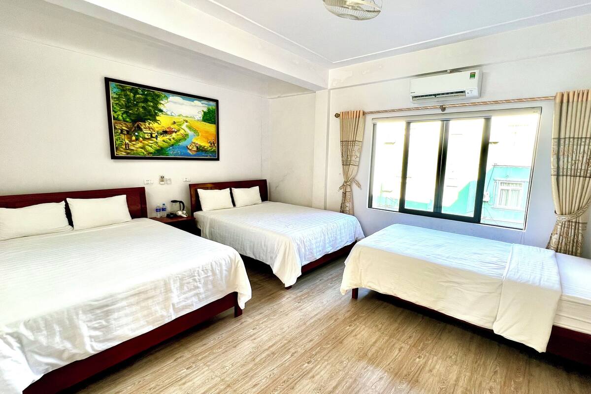 A hotel room with two beds, a painting on the wall, an air conditioning unit, and a window with curtains.
