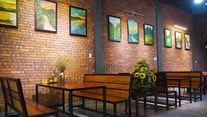 A restaurant with brick walls, wooden benches, and framed landscape paintings. - Thao Nguyen Homestay (Phong Nha)