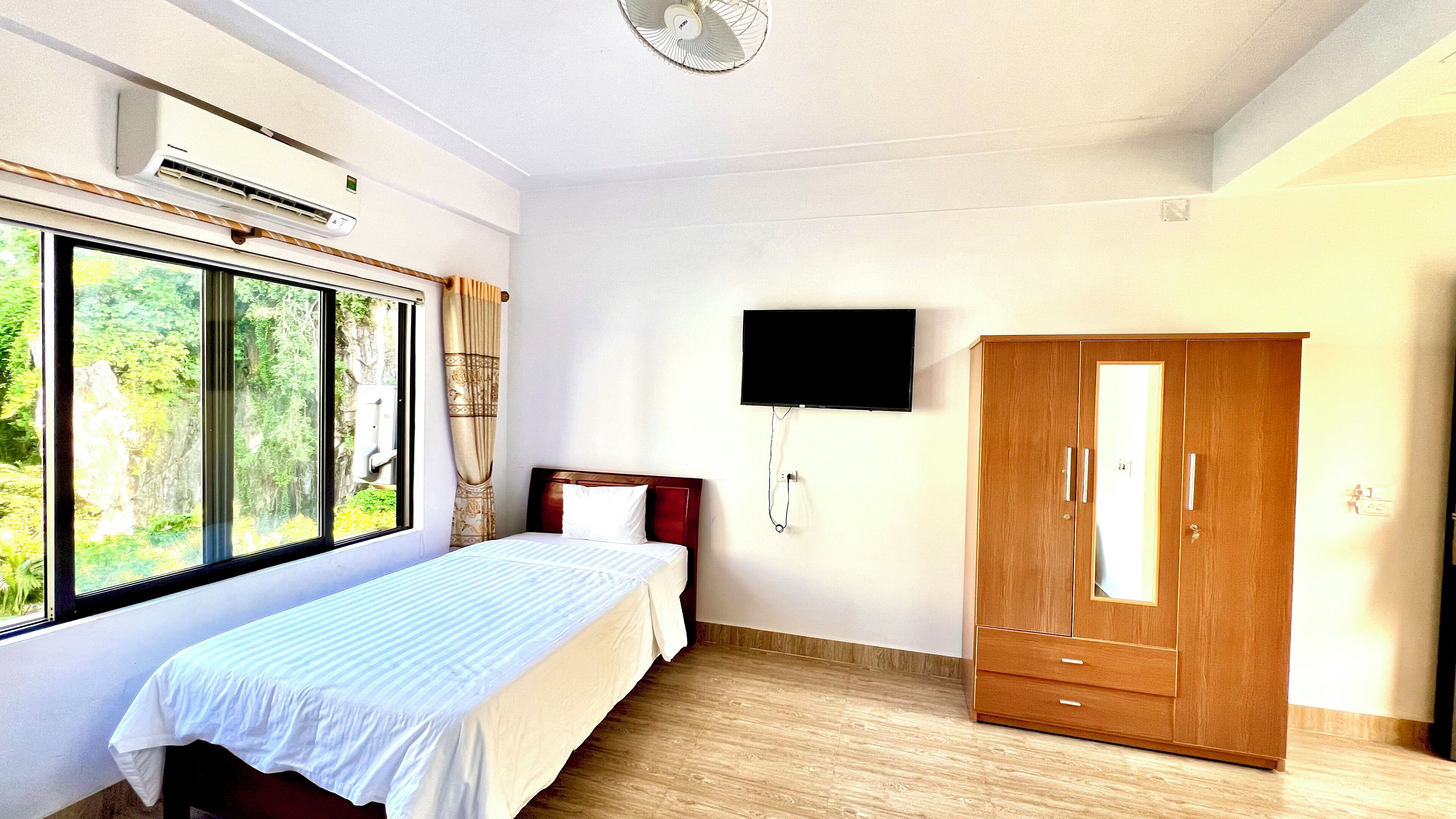 A bedroom with a bed, a wardrobe, a TV, and a window with a view of greenery.