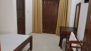 A room with a bed, a wooden table, a chair, a mirror, and a door with curtains.