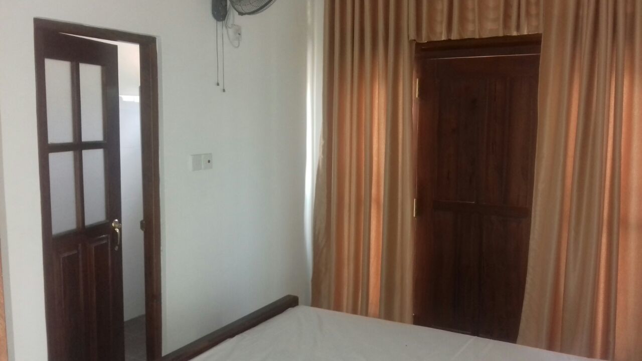 A room with a bed, a wooden door, and a curtain.