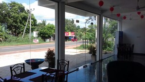A restaurant with a glass partition, outdoor seating, and a view of the street. - Padmasiri Holiday Resort (Anuradhapura)