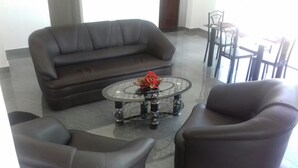 A living room with a dark-colored sofa, a glass coffee table with a red centerpiece, and a dining area with chairs and a table. - Padmasiri Holiday Resort (Anuradhapura)