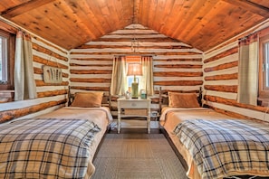 A log cabin room with two beds, a nightstand, a lamp, and a window with curtains. - Macungie Cabin w/ Fireplace Near Bear Creek Skiing (Macungie)