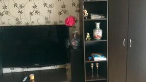 Een woonkamer met een flatscreen-tv, een afstandsbediening, een kleine kaars en een decoratieve vaas op een plank.