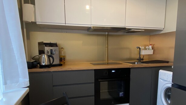 Een compacte keuken met witte kastjes, een koffiezetapparaat, een magnetron en een wasmachine.