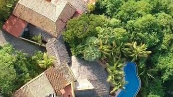Vue aérienne d’une propriété située sur la côte, avec une piscine, plusieurs bâtiments et une végétation luxuriante.