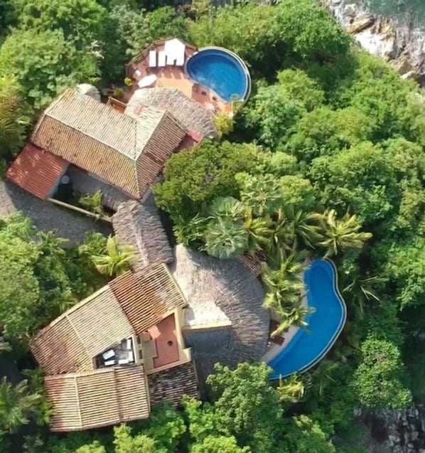 An aerial view of a coastal property with a swimming pool, multiple buildings, and lush greenery.