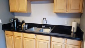 Una cocina con armarios de madera, encimera negra, pileta de acero inoxidable y cafetera.
