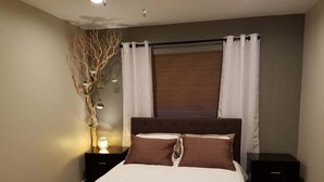 Un dormitorio con una cama, dos mesitas de noche, una lámpara de pared y una ventana con persianas.