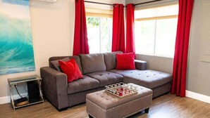 Un salón con un sofá seccional gris, cojines rojos, una mesa de centro de madera y un ventanal con cortinas rojas.