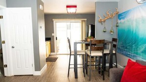 Un salón moderno con comedor, una puerta blanca, una cocina al fondo y un cuadro grande en la pared.
