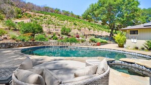 A swimming pool with a stone edge, surrounded by a stone wall and a grassy hillside. There is a wicker lounge chair with cushions. - Sonoma Vineyard Estate - 3bd/2bth (Sonoma)