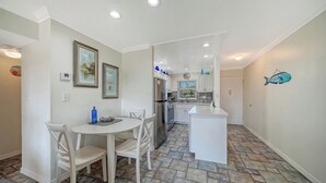 A modern kitchen with white cabinets, a central island, and a dining area with chairs. - Condo # 110 Ground floor unit with quick access to Siesta Beach Amenities (Sarasota)