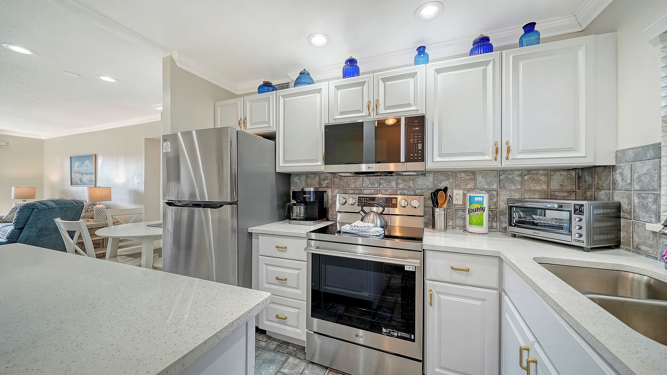 A modern kitchen with white cabinets, stainless steel appliances, and blue decorative vases on the upper cabinets.