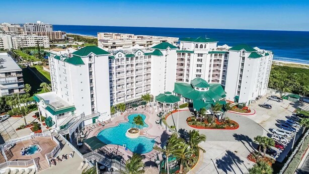 A hotel with multiple floors, a central pool, and a view of the ocean.