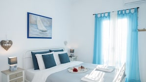 A bedroom with a bed, a nightstand, a wall-mounted shelf, a painting, and a window with curtains. - Mykonos Town Panorama with Private Terrace  (Mikonos)