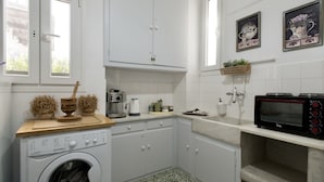 A compact kitchen with white cabinets, a washing machine, a coffee maker, and a microwave. - Mykonos Town Panorama with Private Terrace  (Mikonos)