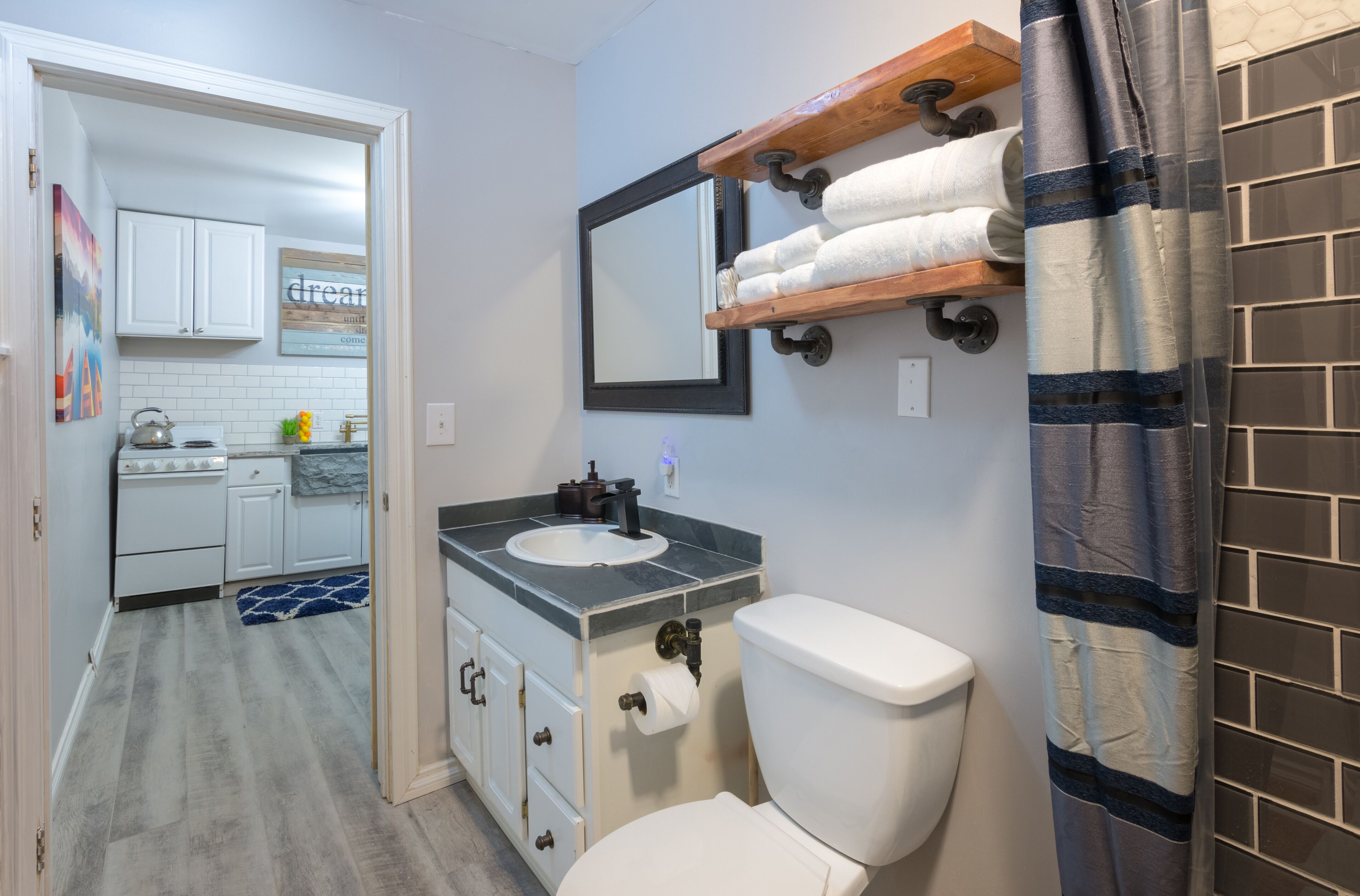 A bathroom with a toilet, sink, and a wooden shelf above the sink.