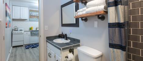A bathroom with a toilet, sink, and a wooden shelf above the sink.