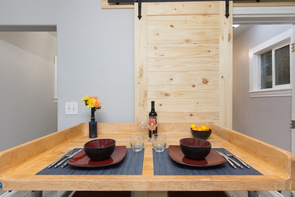 A dining table with two red bowls, two wine glasses, and a bottle of wine.