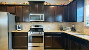 Una cocina con alacenas de madera oscura, electrodomésticos de acero inoxidable, incluyendo un refrigerador, microondas y estufa, y una encimera de granito.